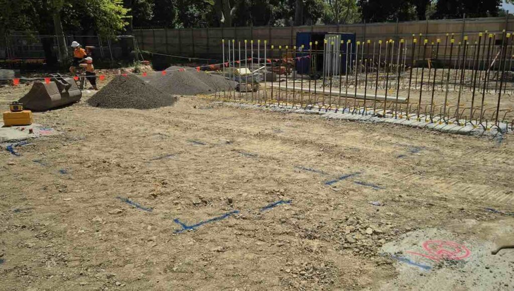 Structural set-out markings on a prepared ground slab with reinforcement bars and a surveyor working in the background, Flemington construction site