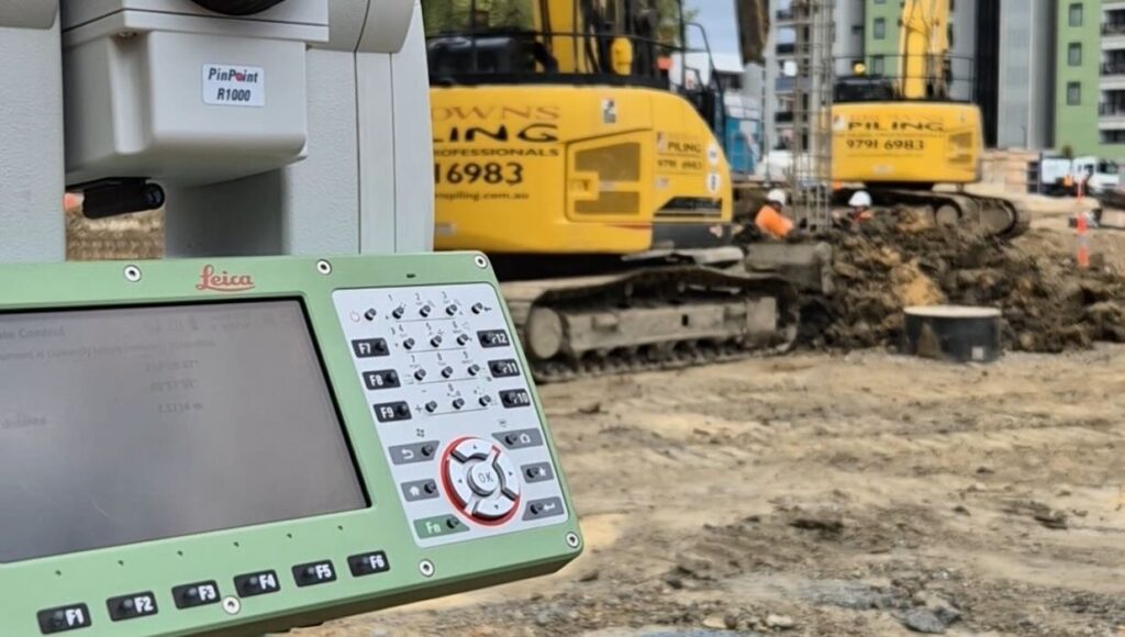 Leica PinPoint R1000 total station on a construction site with piling equipment and excavators in the background, Flemington